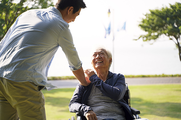 A young man shaking hands with an elderly man on a wheelchair.