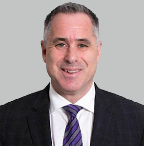 Dr. David Eisen – Dr. David Eisen is photographed from the shoulders up in front of a grey background. He smiles at the camera. He has light-tone skin and black and white short hair. He wears a black suit with a white collared shirt and a purple and blue tie.