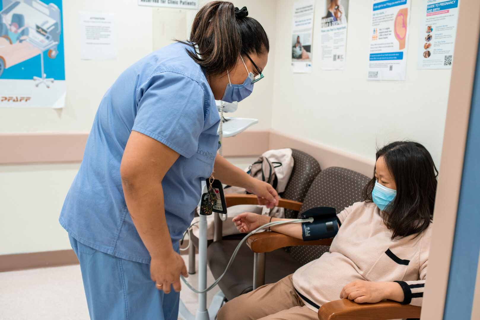 A nurse in a blue uniform checks a patient's blood pressure.