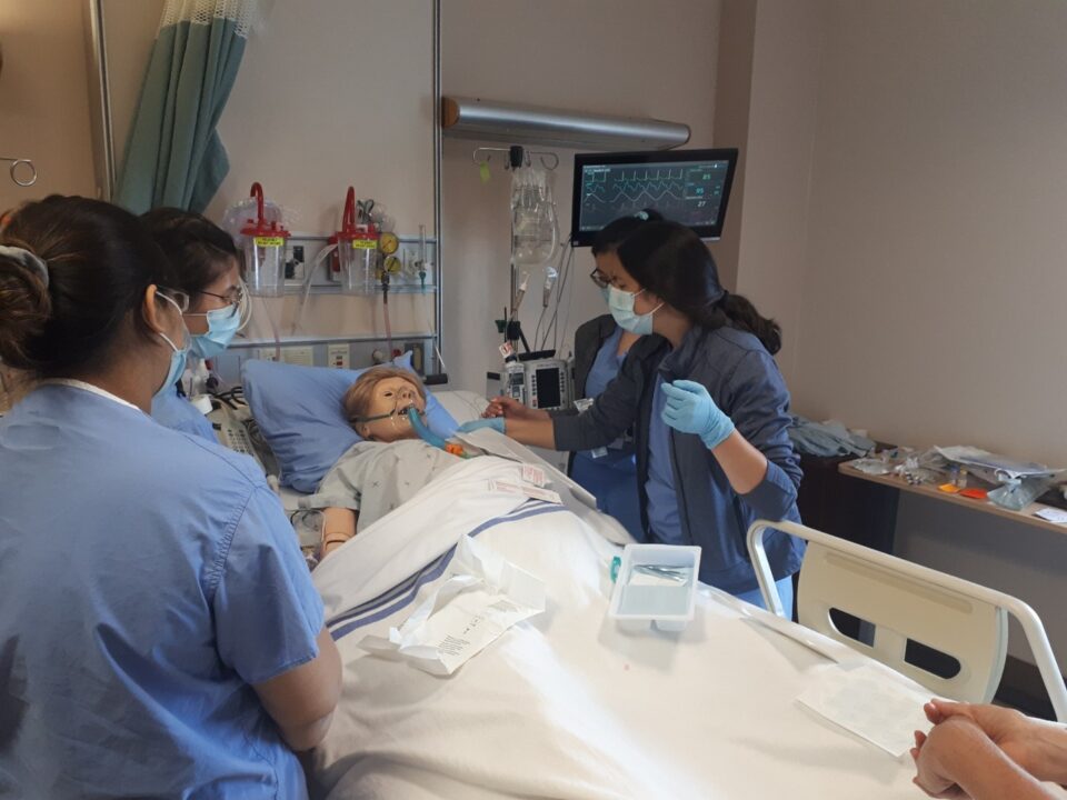 Four nurses assisting a mannequin patient lying on a bed during a simulation.