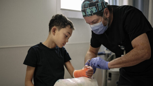 A boy with a cast on his arm receiving care from a physician.