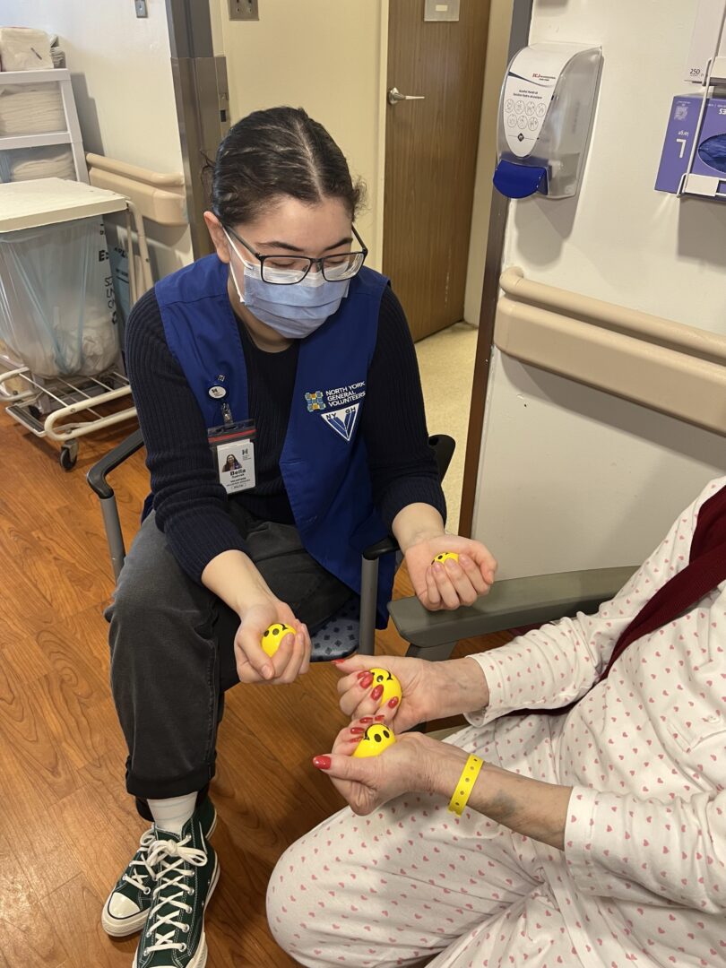 NYGH volunteer in blue vest is assisting patient using yellow stress balls.