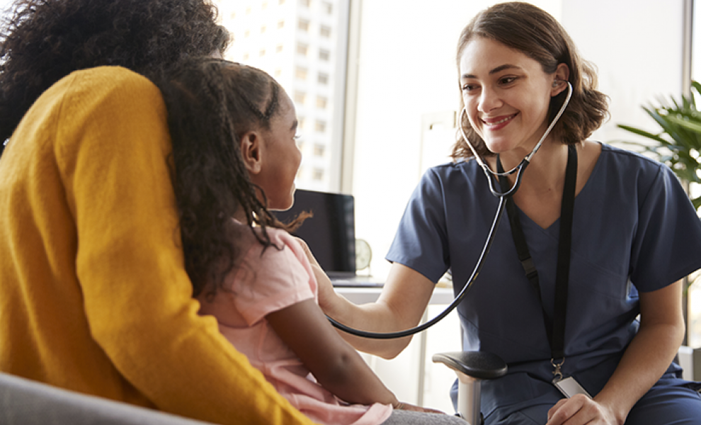 A smiling nurse listening to a girl's heartbeat using a stethoscope