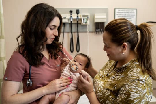 A female family doctor holds a small baby with the mother holding the baby's hand.